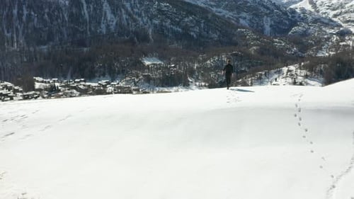 Person walking over snow covered mountain edge and looking over valley