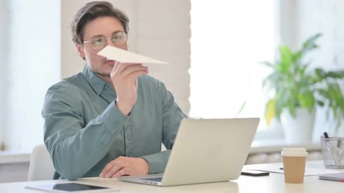 Mann mittleren Alters mit Laptop fliegendes Papierflugzeug