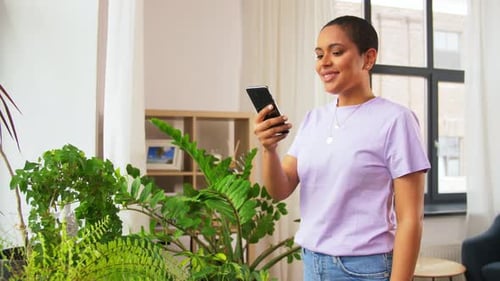 Woman Using Smartphone Near Indoor Plants at Home