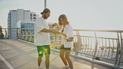Man Helping Woman Skateboard on Bridge at Sunset