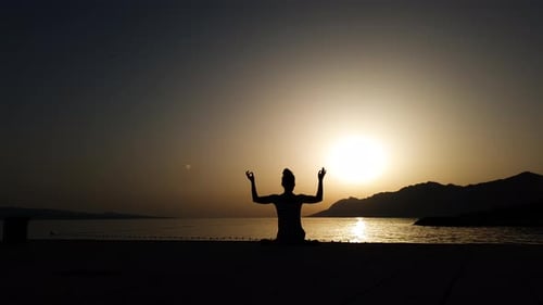 Yoga woman meditating at sunset by the ocean