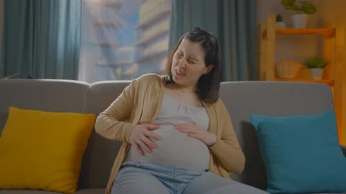 Schwangere Frau sitzt auf der Couch und hat Wehen, Schmerzen