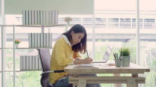 Woman at Desk Writing in Notebook with Laptop