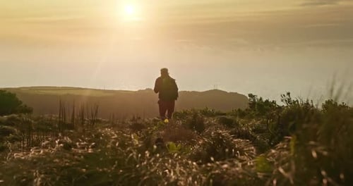 Person Hiking at Sunset on Grassy Hill