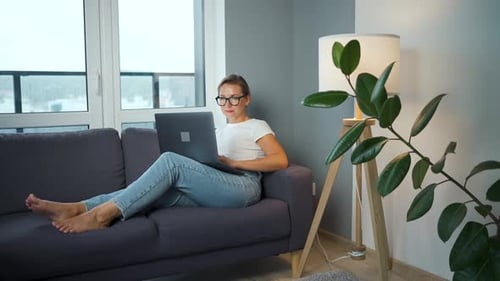 Woman Works on Laptop Relaxing on Sofa
