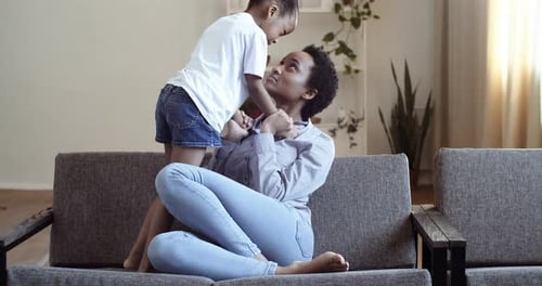Afroamerikanische Mutter mit Tochter auf der Couch Umarmt zärtlich Kuscheln kommuniziert sprechenden Scherz