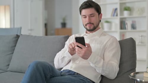 Excited Man Celebrating with Smartphone on Couch