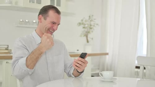Excited Man Using Smartphone in Modern Kitchen