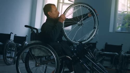 Side View of One American Male Workers in a Workshop at a Factory Making Wheelchairs Sitting at a