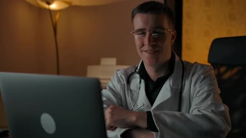 Doctor Smiling at Laptop in a Dark Room