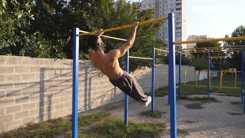Strong Sporty Man Showing Some Gymnastics Stunts on Horizontal Bar Outdoor