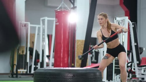 A Sporty Woman Hits a Tire with a Hammer