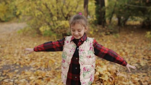 A Little Girl Plays with Yellow Leaves and Falls Into Them