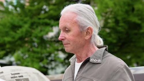 Handsome Grayhaired Man Sitting on the Bench Early in the Morning and Reading Newspaper in Park