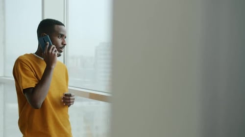 Cheerful African American Student Chatting on Mobile Phone Watching City From Panoramic Window