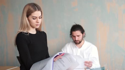 Young Woman Office Worker Close Up Work with Papers and Her Male Collegue at the Background