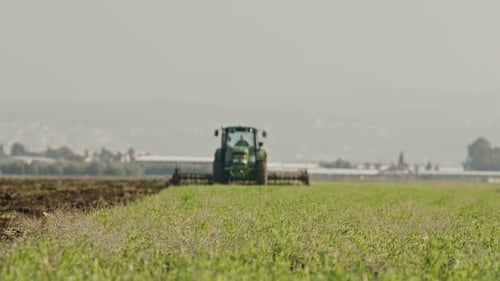 Tractor cultivating a green field in slow motion.