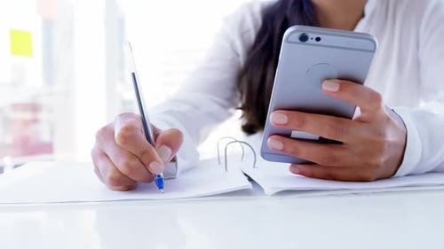woman using smartphone and taking notes