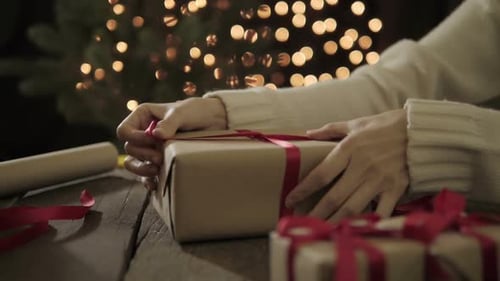 Hands Wrapping a Christmas Gift With Red Ribbon