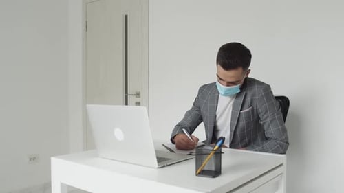 Young Adult Working on Laptop While Wearing Mask