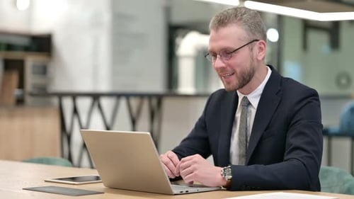 Cheerful Young Businessman Talking on Video Call on Laptop in Office
