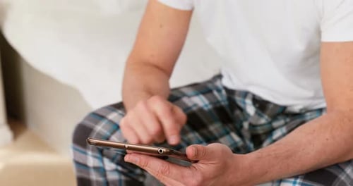 Man Smiling Using Smartphone Device in Bedroom