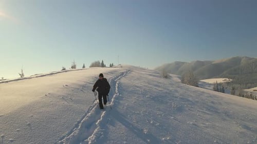 Hiker with Backpack Walking on Snowy Mountain Hillside on Cold Winter Day