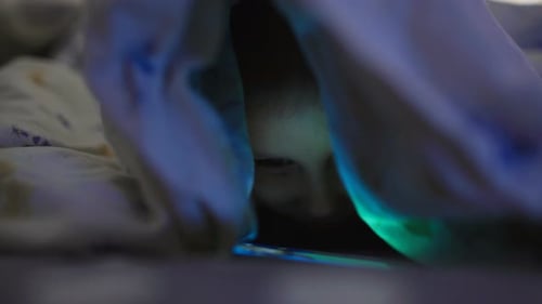 Petite fille jouant et regardant un smartphone sous couverture