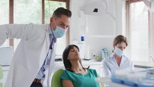 Caucasian male dentist with face mask examining teeth of female patient at modern dental clinic