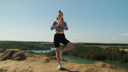 Mujer delgada con top gris y pantalones cortos deportivos negros practica yoga al aire libre en la naturaleza