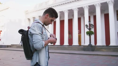 Attractive Young Handsome Man Tourist with Backpack Walking in City Center and Taking Photos on