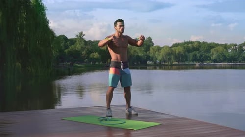 Muscular Man Exercising with Resistance Band Near Lake