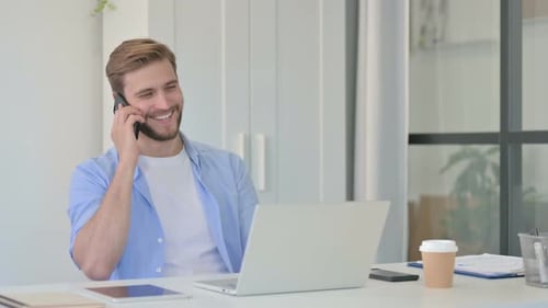 Young adult talking on cell phone at desk
