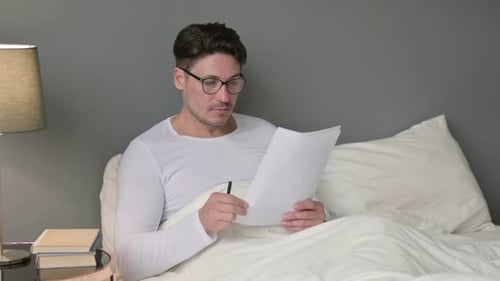 Man Reads Document in Bed at Home