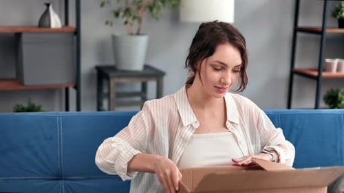 Happy Young Brunette Woman Opening Cardboard Box Internet Store Purchase Received Sitting on Couch