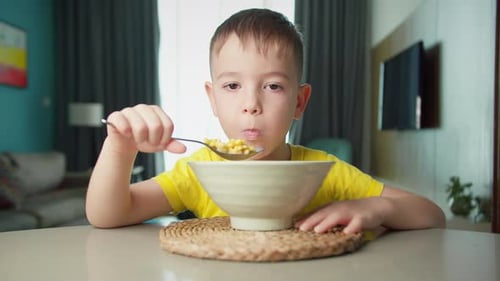 Hungry Child Cute Boy Sits at the Dinner Table Eats Corn Flakes with Milk with an Appetite of