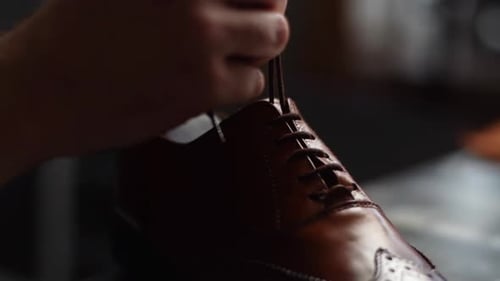 Closeup de sapateiro masculino amarrando cadarços em sapatos de couro marrom claro reparados e polidos