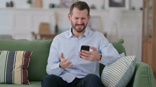 Man Reacts Angrily to Phone While Sitting