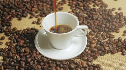 Pouring Coffee Into Cup Surrounded by Coffee Beans