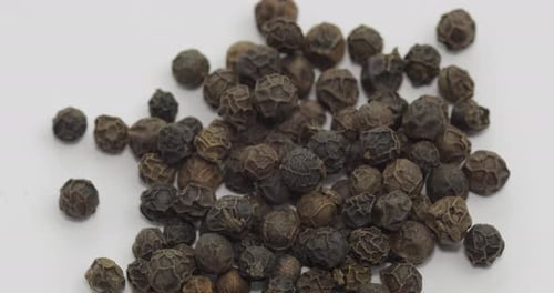 Heap of aromatic Black Peppercorns on White Surface