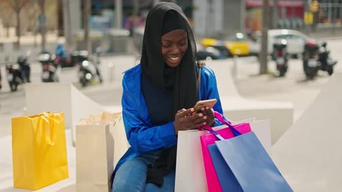 Muslim Female Shopaholic Using Smartphone on Bench