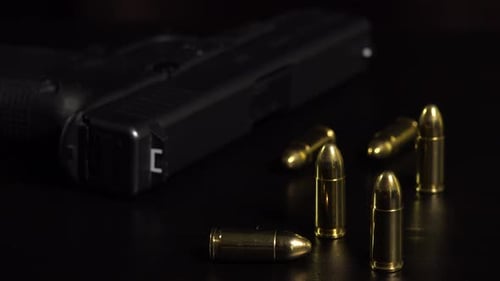 Nahaufnahme von Kugeln und einer Waffe auf einem schwarzen Tisch