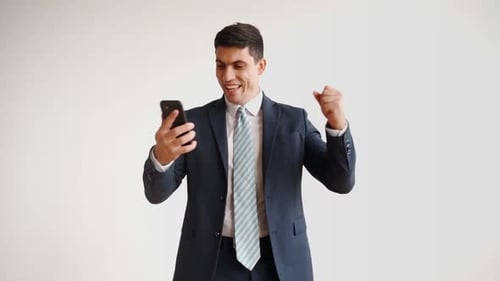Happy Male Office Worker in Formal Clothes Uses Mobile Phone Rejoices in Victory