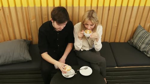 Young Couple Is Drinking Coffee and Talking While Sitting at the Cafe