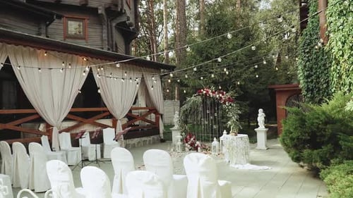 Wedding Arch with Red Flowers and White Chairs Lamp Garland Over the Ceremony Near Restaurant Slow