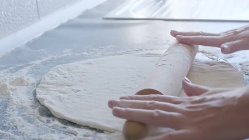 Hands Rolling Dough with Flour in Kitchen