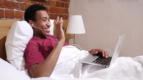 Young Adult Using Laptop in Bed for Video Call