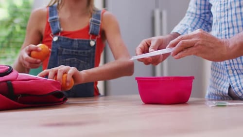 Girl and Adult Packing Lunch at Kitchen Table