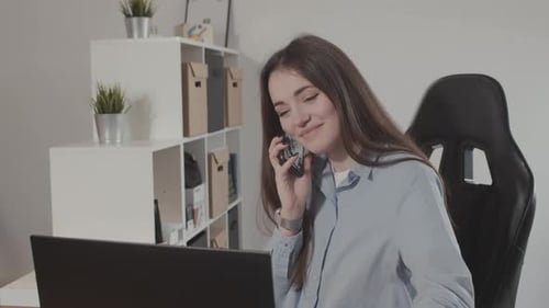 Young Woman Answering Phone While Working on Laptop