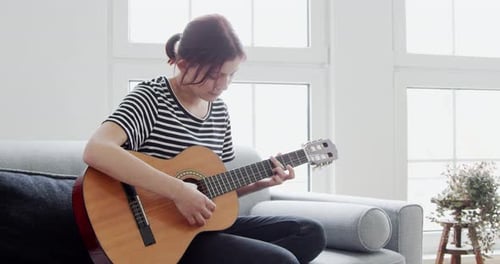 Girl Plays Guitar on Couch Indoors